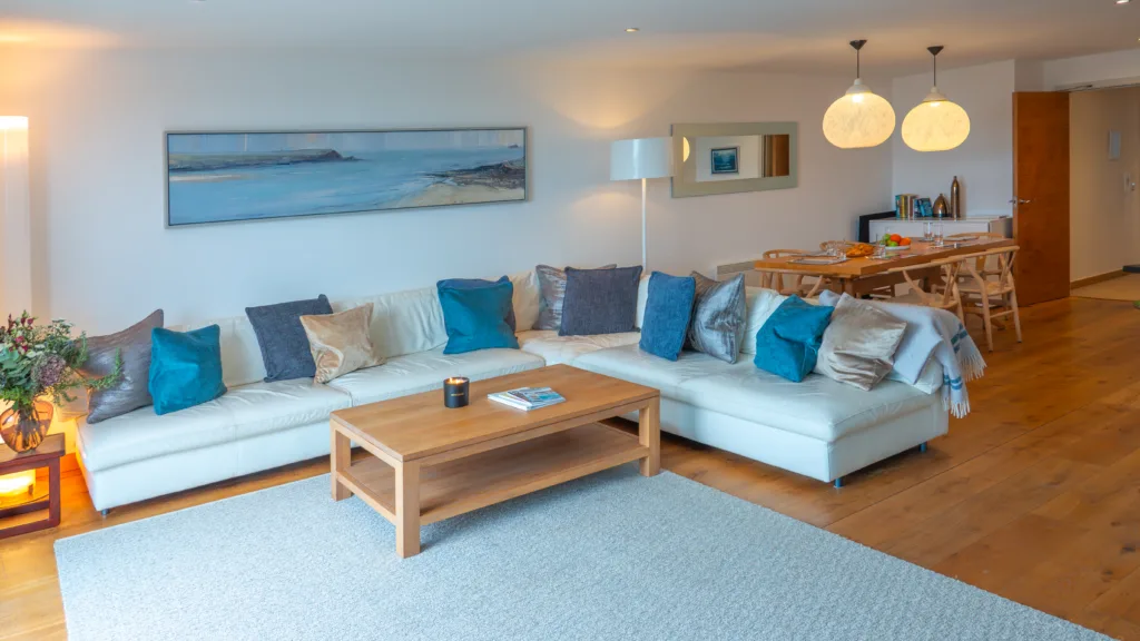 Dining and living area. Large L shaped sofa surrounding the wooden coffee table in the living area. Behind is the dining table and chairs. There is a doorway at the back leading to other areas of the apartment.