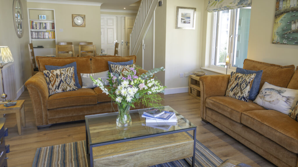 Villa living area. Two sofas and a coffee table at the front of the image. Behind the sofa is a dining table. Next to the dining area is a staircase leading up to the upstairs area.