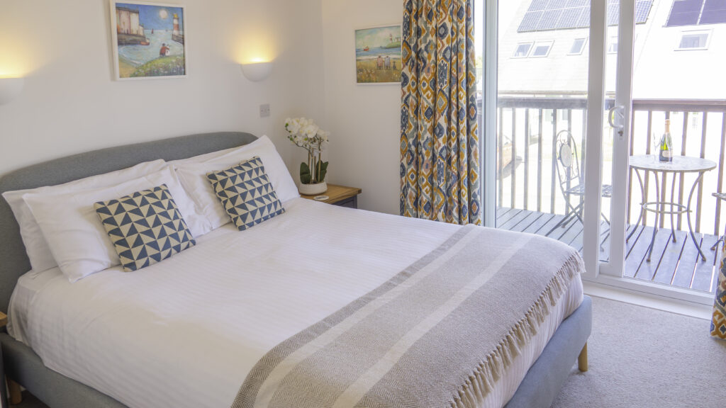 Villa 12a bedroom. Double bed with bedside table. Sliding doors leading out to the balcony. Balcony is furnished with two chairs and a table.