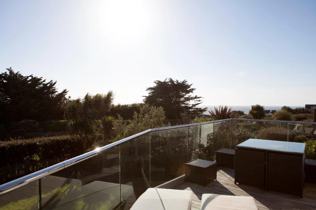 Villa 35 balcony and view. Balcony is furnished with sunlounges and a table with stools. The villa gardens below. In the distance there is the sea.