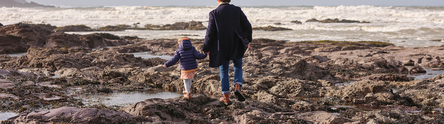 Christmas in Cornwall 1 Christmas. A man and a child walking over the rocks on and the rockpools. Waves in the background.